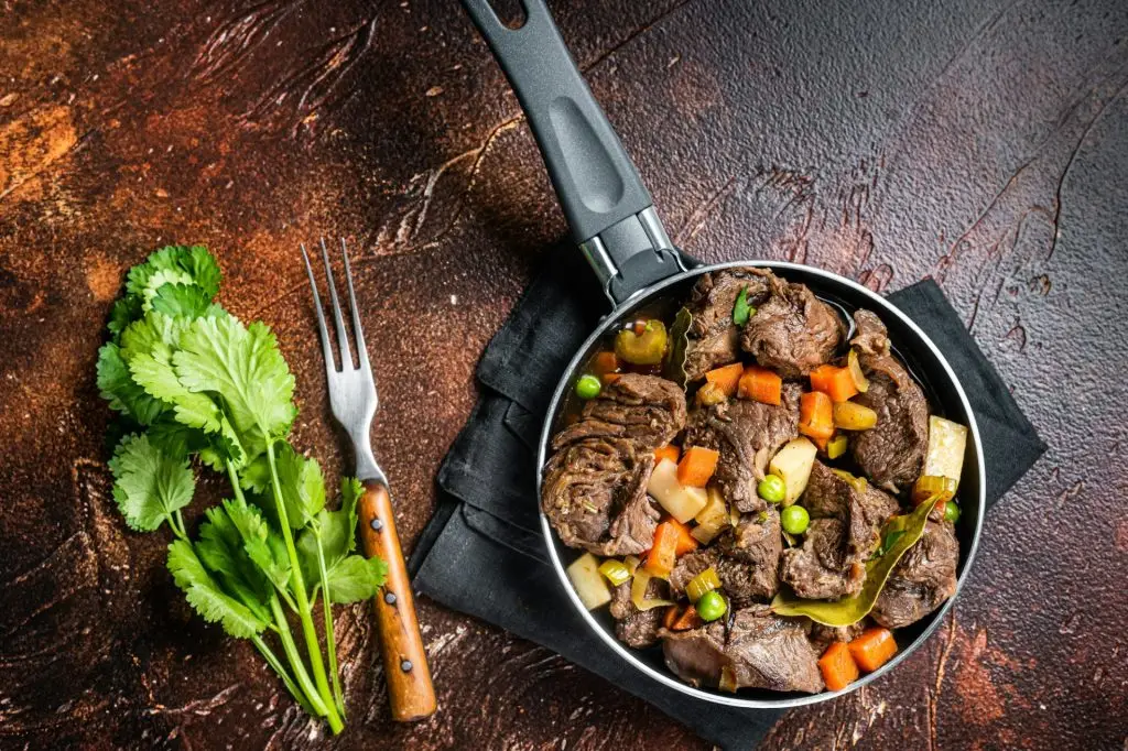 Irish stew with beef meat, potatoes, carrots and herbs in a skillet. Dark background. Top view