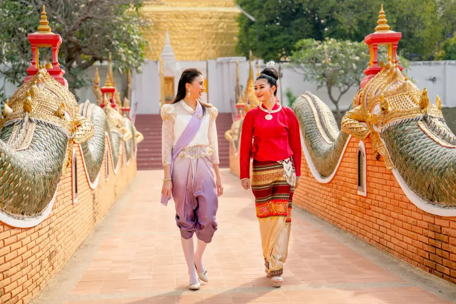 Thai women with traditional dress walk together and talk on walkway of famous temple
