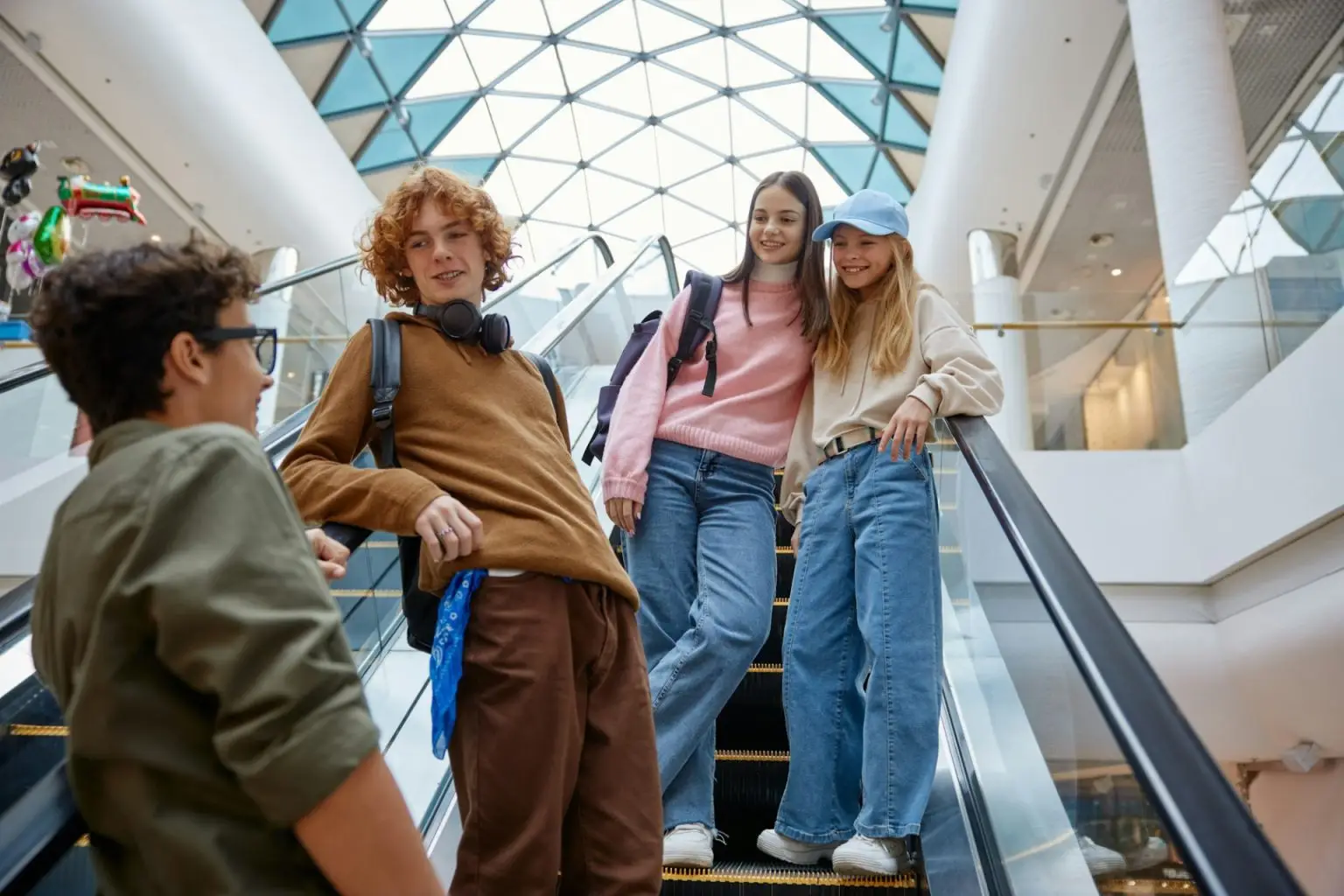 Happy teenage friends team moving staircase at shopping mall