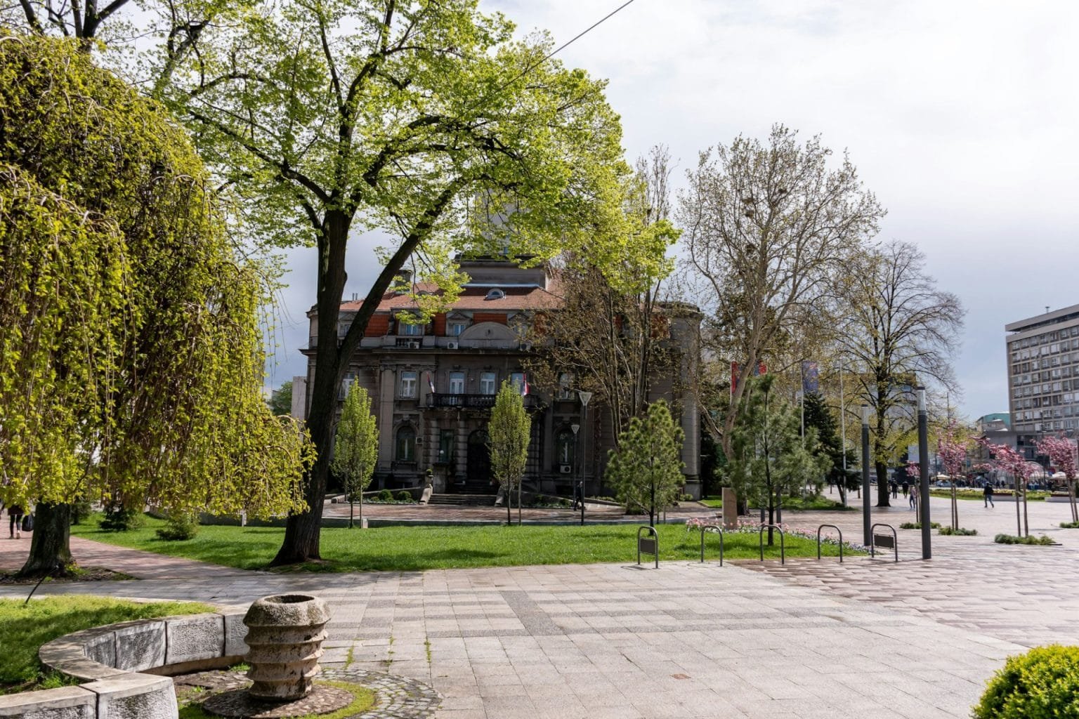 Beautiful shot of the Nis Town Hall behind sunny trees and green land in downtown Nis, Serbia