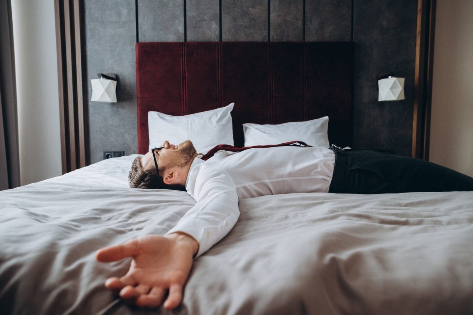 Exhausted businessman resting on bed after long air flight, jet lag.