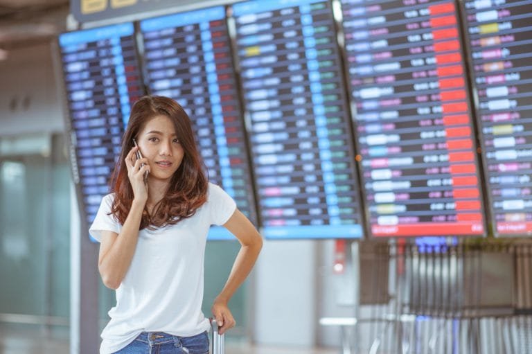woman in international airport using her mobile phone near the flight information board,
