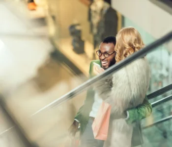 stylish young couple riding escalator and embracing at shopping mall