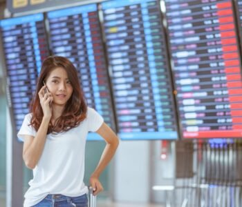 woman in international airport using her mobile phone near the flight information board,